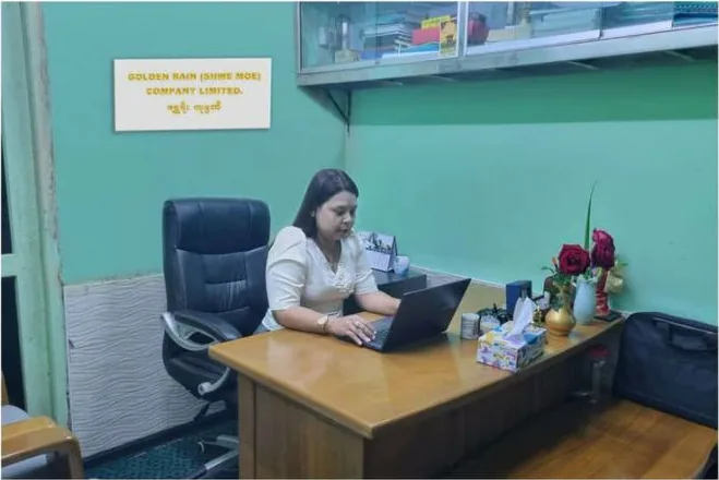 A member of staff working at a desk beneath the Golden Rain (Shwe Moe) Company Limited nameplate