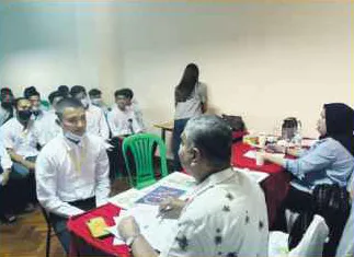 Candidates seated in a room facing a table where an interviewer looks through documents