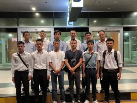Twelve men in white and dark shirts standing in two rows inside a terminal hall at night