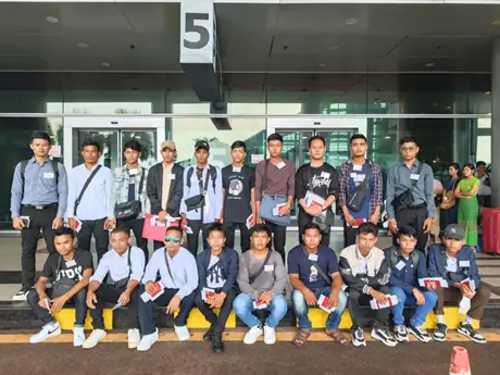 A large group in two rows outside a terminal entrance, most wearing name badges and holding papers
