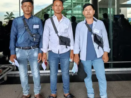 Three men standing outside a terminal in daylight, name badges pinned, papers and face masks in hand